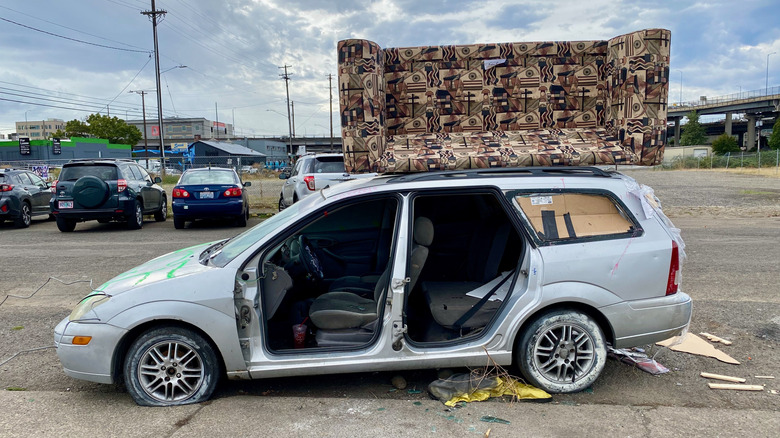 An abadoned first generation Ford Focus wagon with a couch on the roof