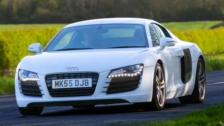 A white Audi R8 driven on road with its LED headlights turned on.