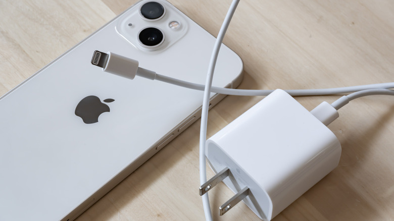 White iPhone 12 lying face down with its charger by its side