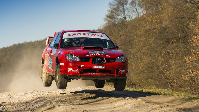 Front 3/4 view of a hawkeye Subaru WRX STI rally car on rally stage, mid-air, red exterior with decals