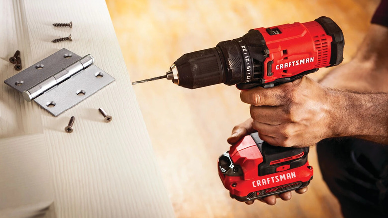 person using a Craftsman half-inch cordless drill to install door hinges
