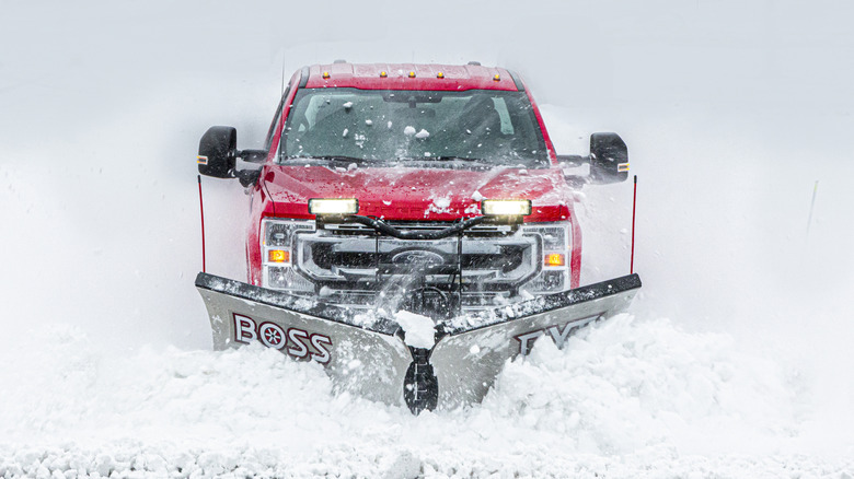A red Super Duty Ford truck plowing through snow.
