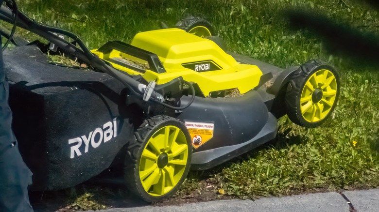 A person pushing a Ryobi lawn mower on grass.