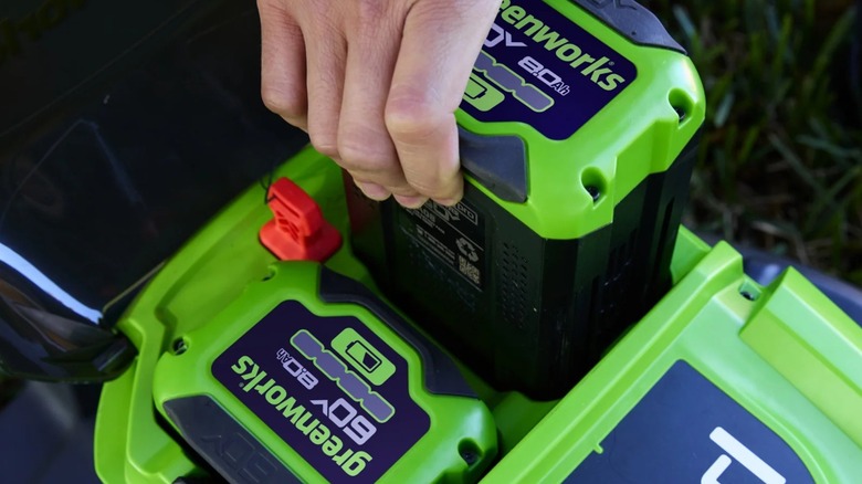 A person holding a Greenworks battery in a lawn mower.