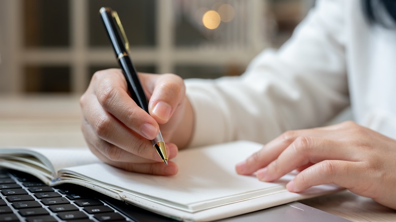 Creating a list with a pen and paper while looking at a laptop