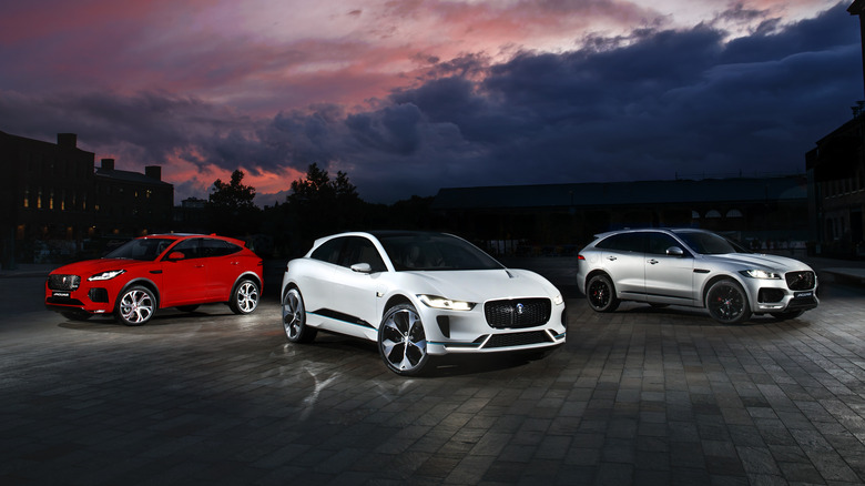 Jaguar SUVs parked outside under cloudy night sky, red E-Pace on the left, white I-Pace in the middle, silver F-Pace on the right