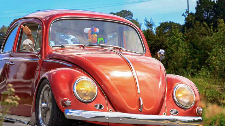 Volkswagen Type 1 Beetle with aftermarket wheels and lowered suspension driving on road, front-view