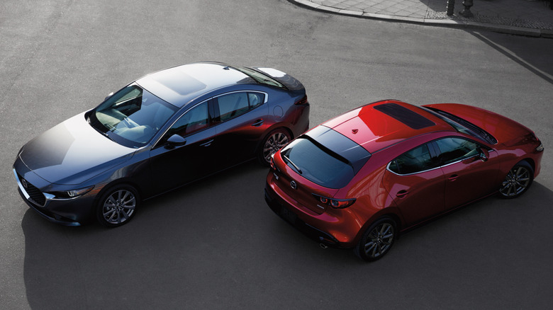 A gray Mazda6 and a red Mazda3 parked side by side on a city street.