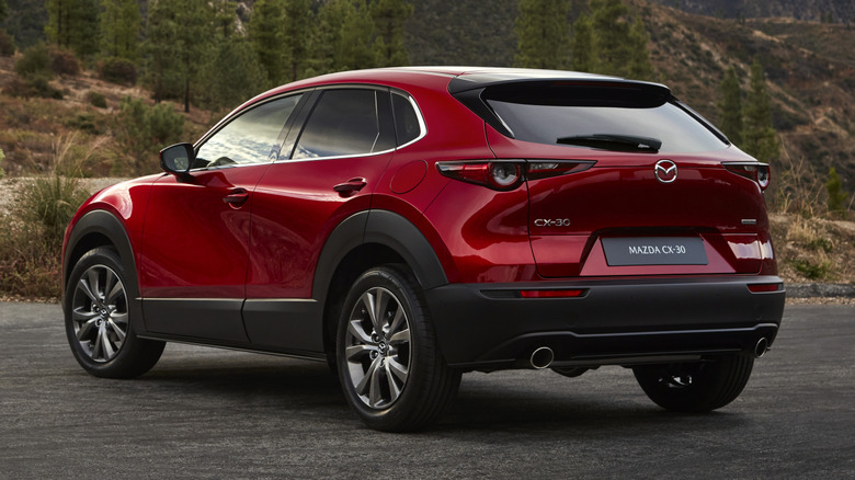 A rear quarter view of a red Mazda CX-30 parked on a hillside with trees in the background