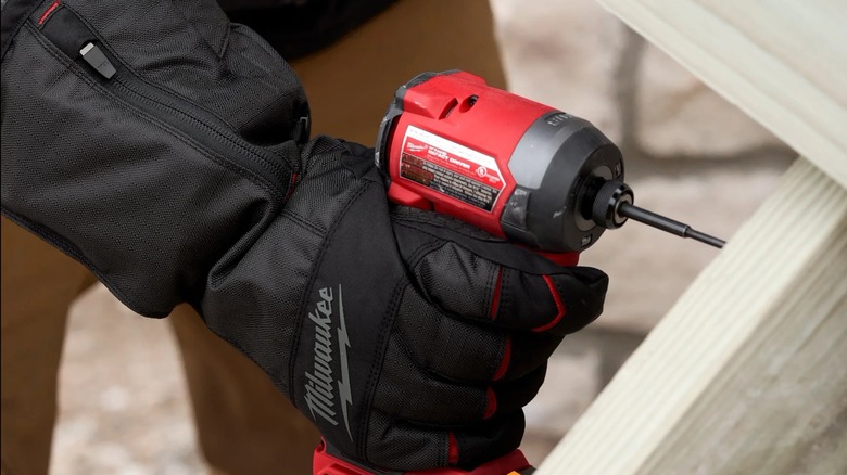 A Milwaukee drill being held by someone wearing heated gloves and drilling wood