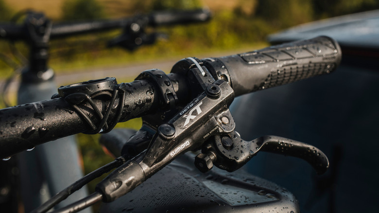 A close up photo of a Shimano XT brake lever on handles bars with water droplets on it.