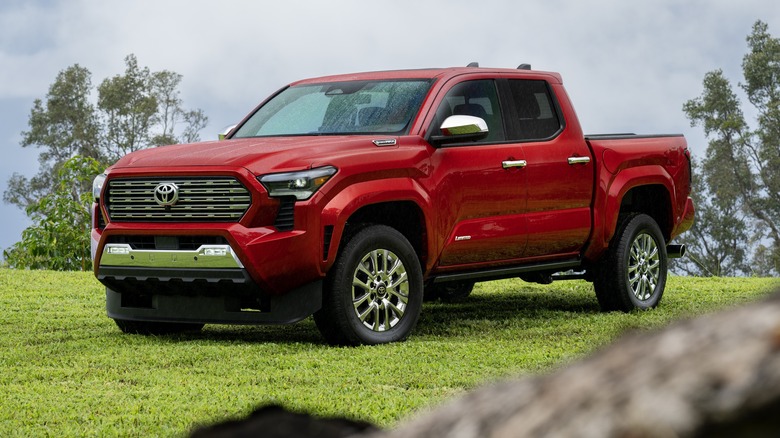 Red 2025 Toyota Tacoma Limited parked on grass with trees in the background