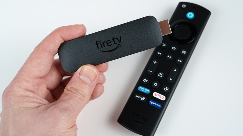 Person holding Fire TV stick with remote control in background
