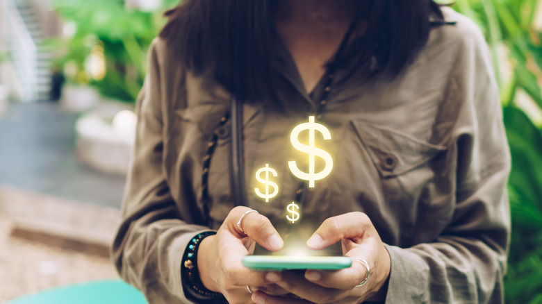 A woman holding a silver cell phone with yellow dollar signs floating above it