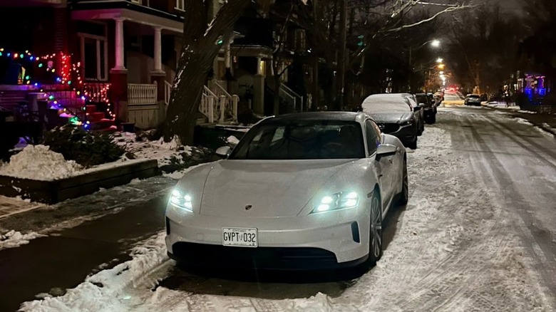 A white Porsche Taycan all-electric car parked on a snowy residential street at night.
