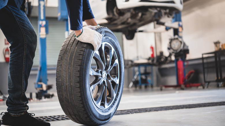 Mechanic moving tire toward car on lifts