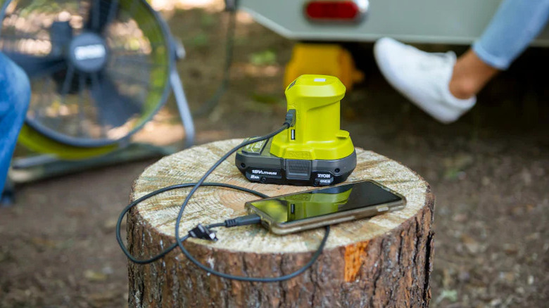 Ryobi One+ 18V Power Source charging a phone on a tree stump