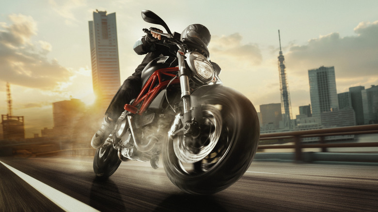 A motorcyclist speeds along a city road at sunset.