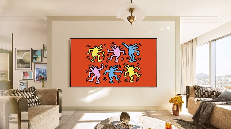 A large Samsung OLED flatscreen TV in a white living room with Keith Haring art on it.