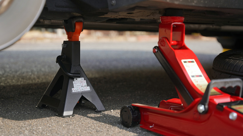 A floor jack and a jack stand holding up a car on pavement.