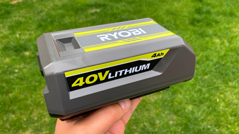 A person holds a 40V Ryobi battery in front of grass