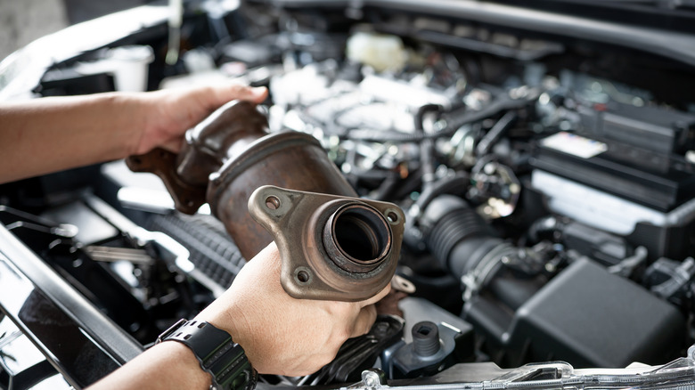 Close-up of technician inspecting used catalytic converter over an open engine bay