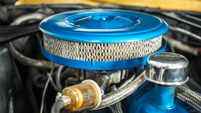 Close-up of single-barrel carburetor and round air filter on a car engine