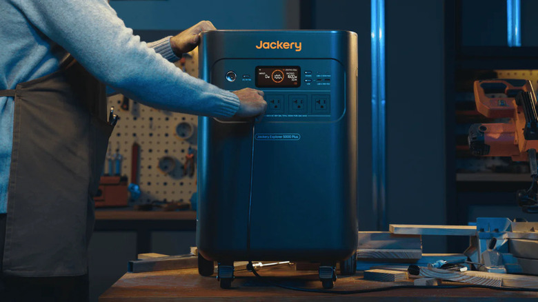 Hand plugging in devices to Jackery battery generator inside a workshop