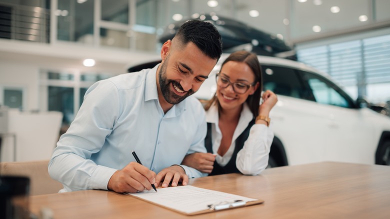 A couple joyfully signing documents at a dealership