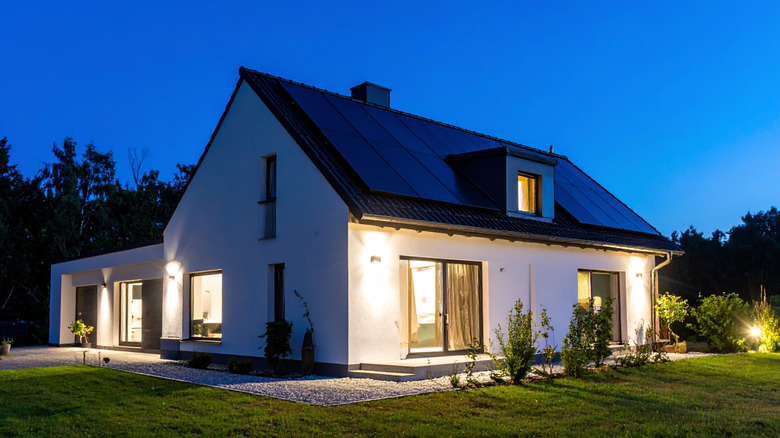 An illuminated home with solar panels on the roof at dusk