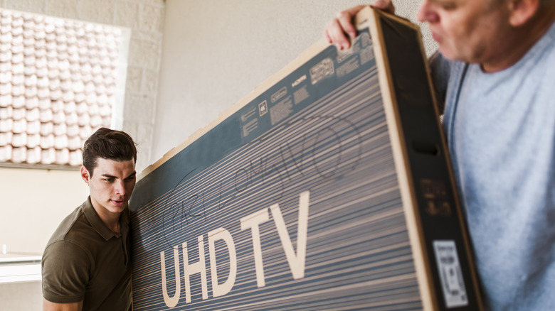 Two persons carrying a TV box