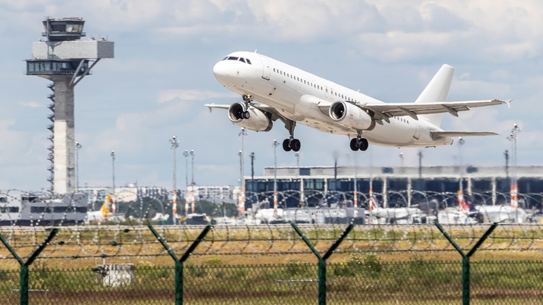 White commercial jet landing at Berlin airport with ATC tower in the background