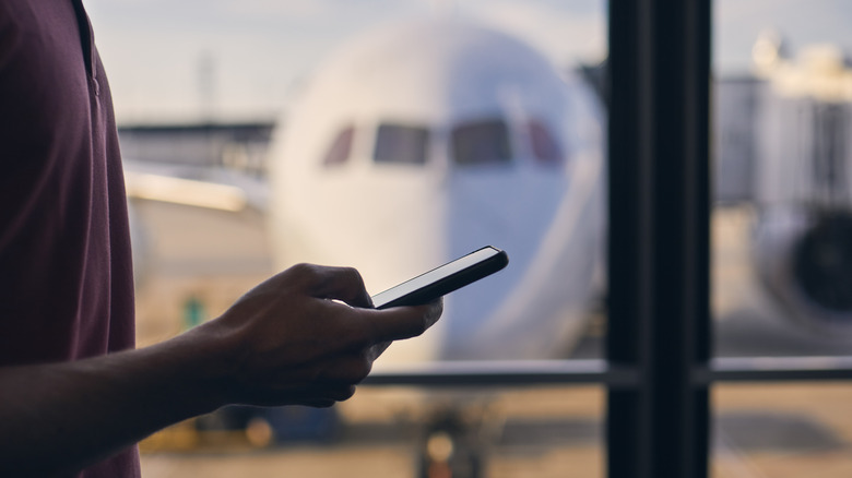 Person holding smartphone with an airplane in the background
