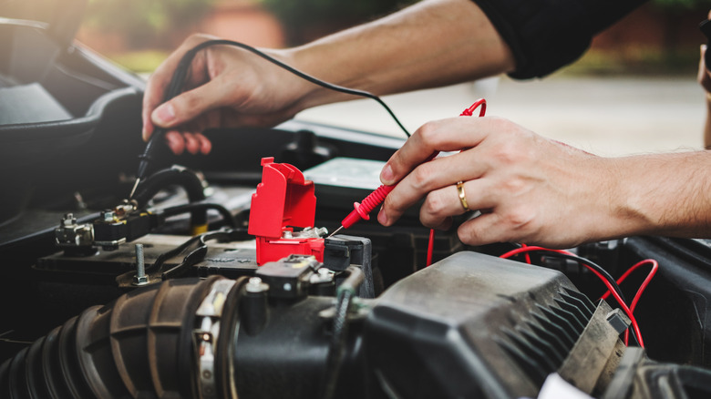 Pair of hands testing car battery voltage
