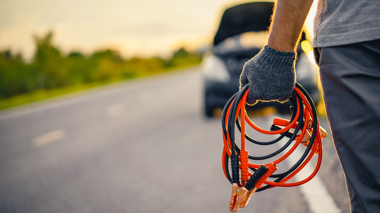 Man holding jumper cables facing car with an open hood