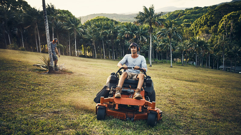 An adult man using a riding land mower with beautiful trees behind