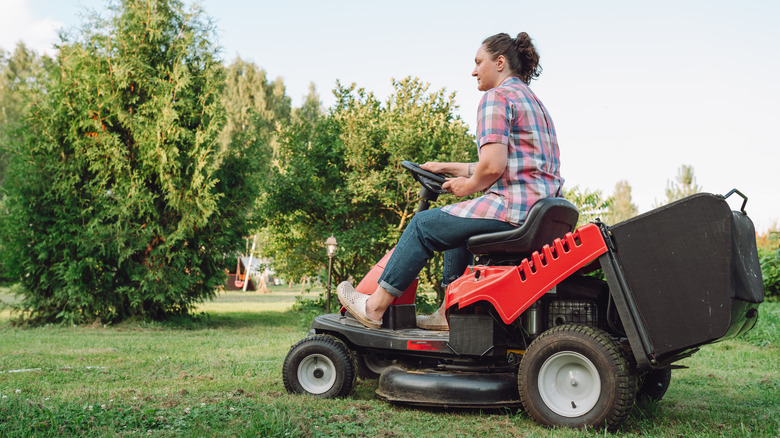 An adult woman driving a lawn mower