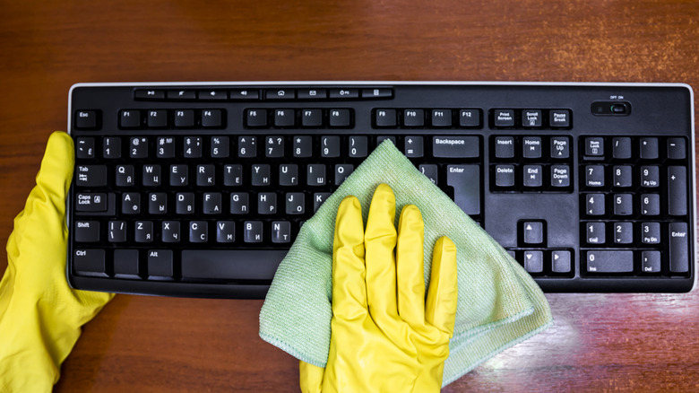 rubber gloved hands using a cloth to clean a keyboard