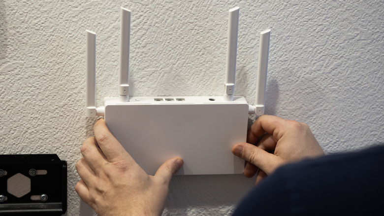 A person installing a white wireless router with 4 antennae on a white wall. Only the hands of the person are shown.