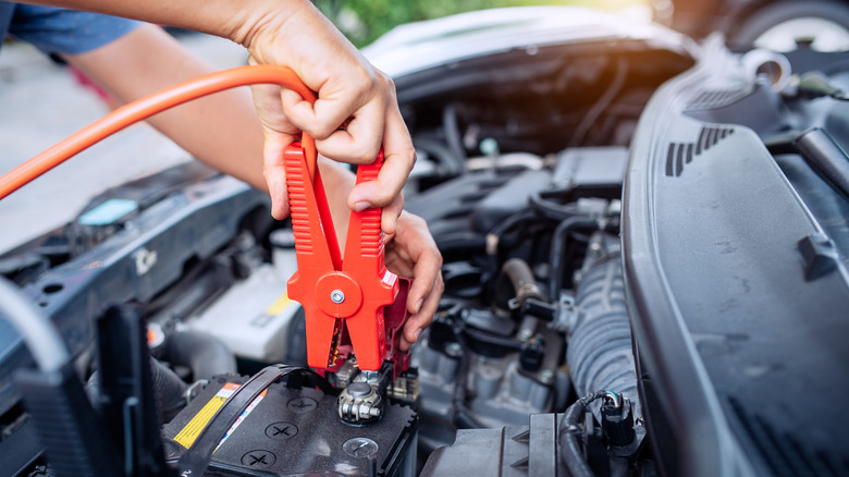 A person attaching jumper cables to a car battery