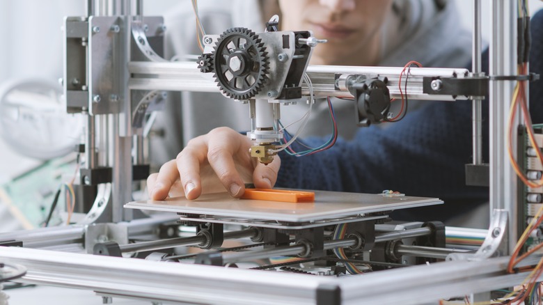 A person holding an orange 3D printed object on a 3D printer base plate.
