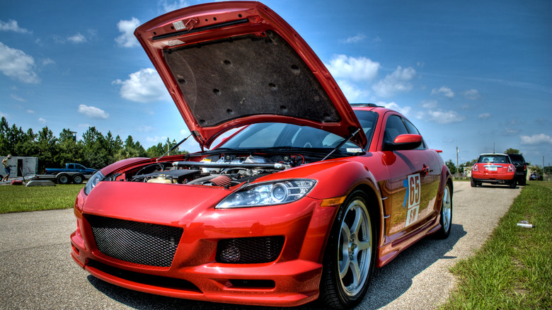 A heavily modified red Mazda RX-8 parked on the road with its hood open.