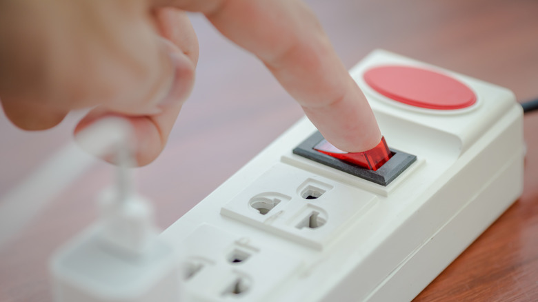 Person using index finger to turn on a power strip
