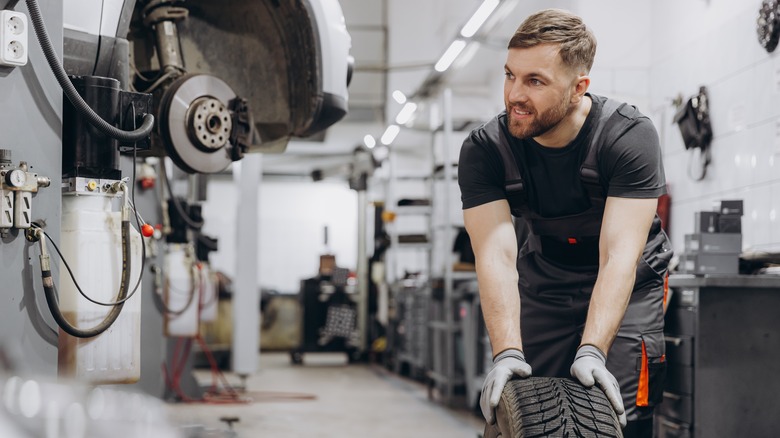 A mechanic rolls a replacent tire toward a car being serviced at the repair shop