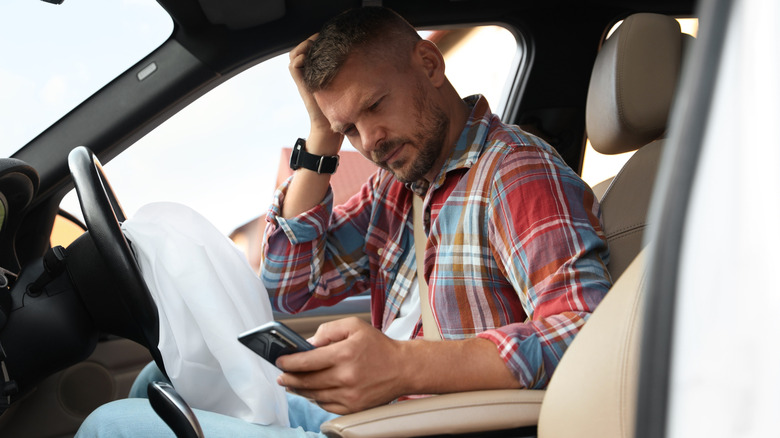A man who appears uncomfortable in the driver seat with a deployed frontal airbag visible