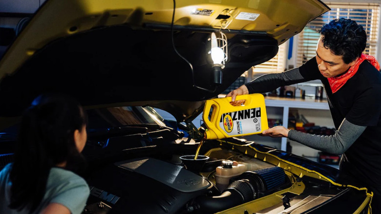 people adding engine oil to a car