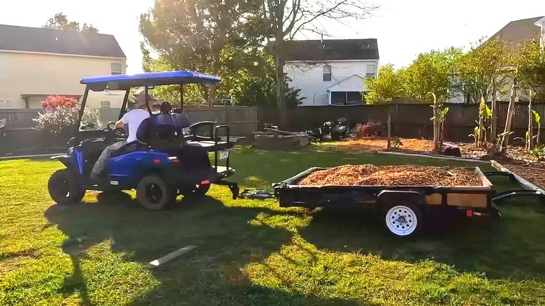 A Man Using A Golf Cart To Tow A Trailer Full Of Mulch