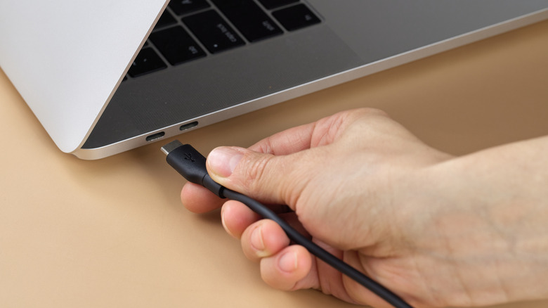 Hand plugging in USB-C cable to laptop power port