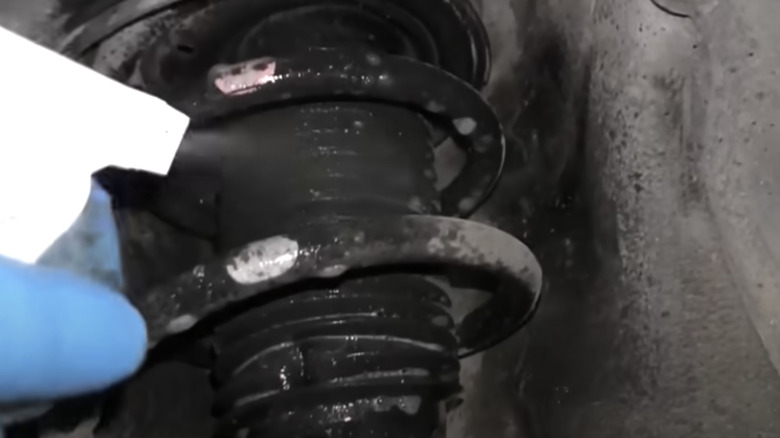 A gloved hand uses a spray bottle to coat a suspension strut