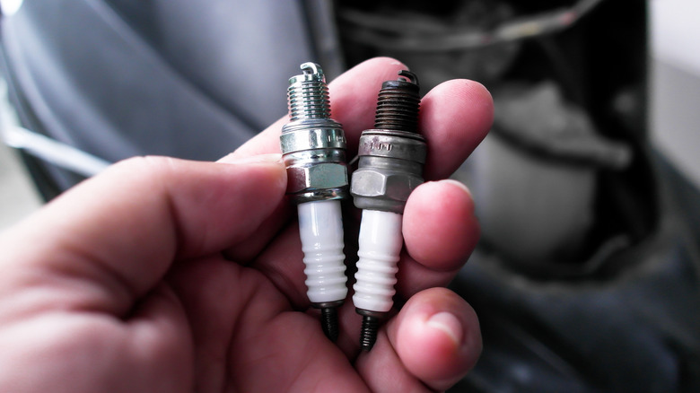 A person holding two spark plugs, one new, and one used.
